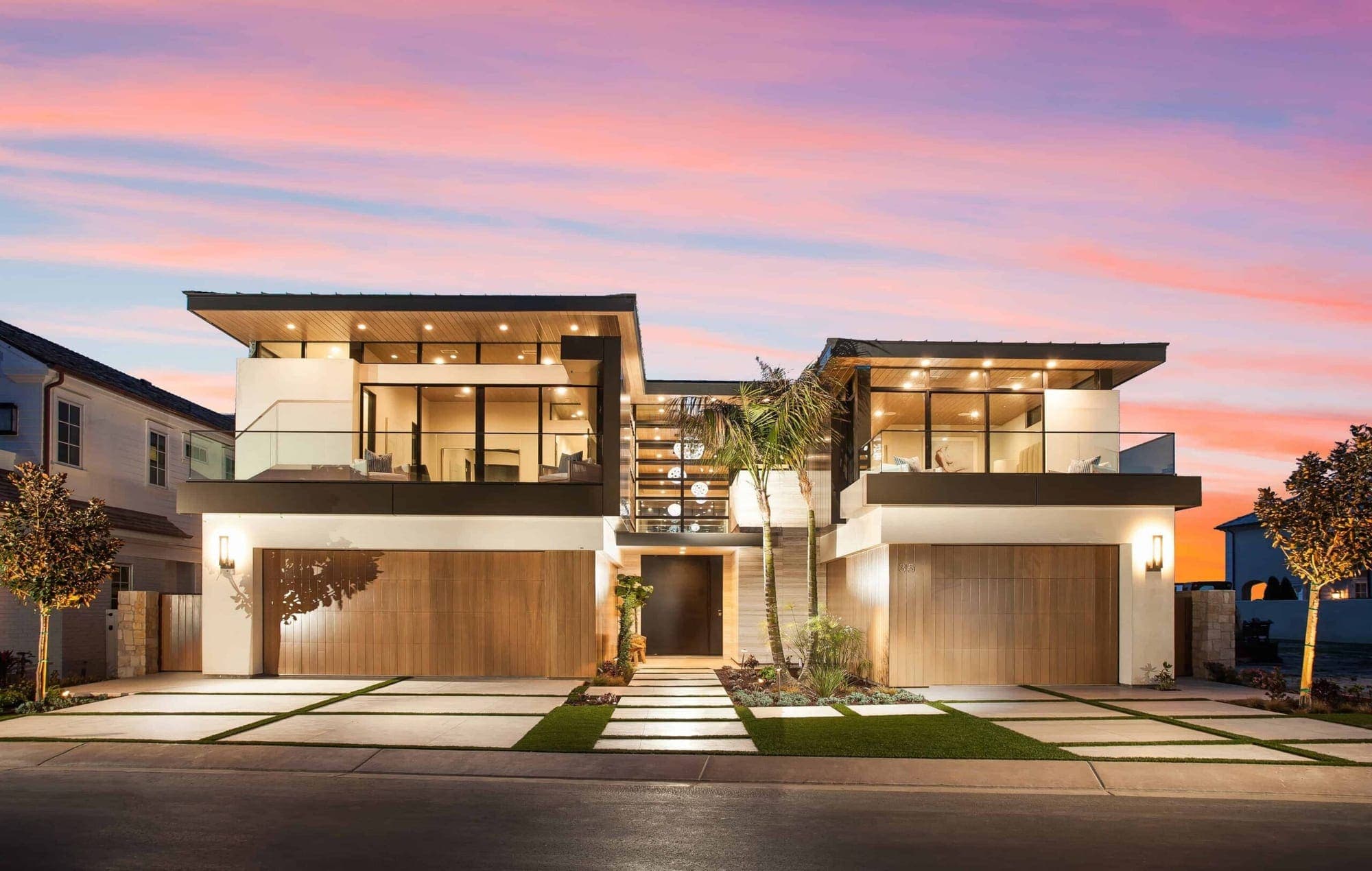 A modern Dana Point home at dusk with warm wood, glass, and a pink sunset sky.