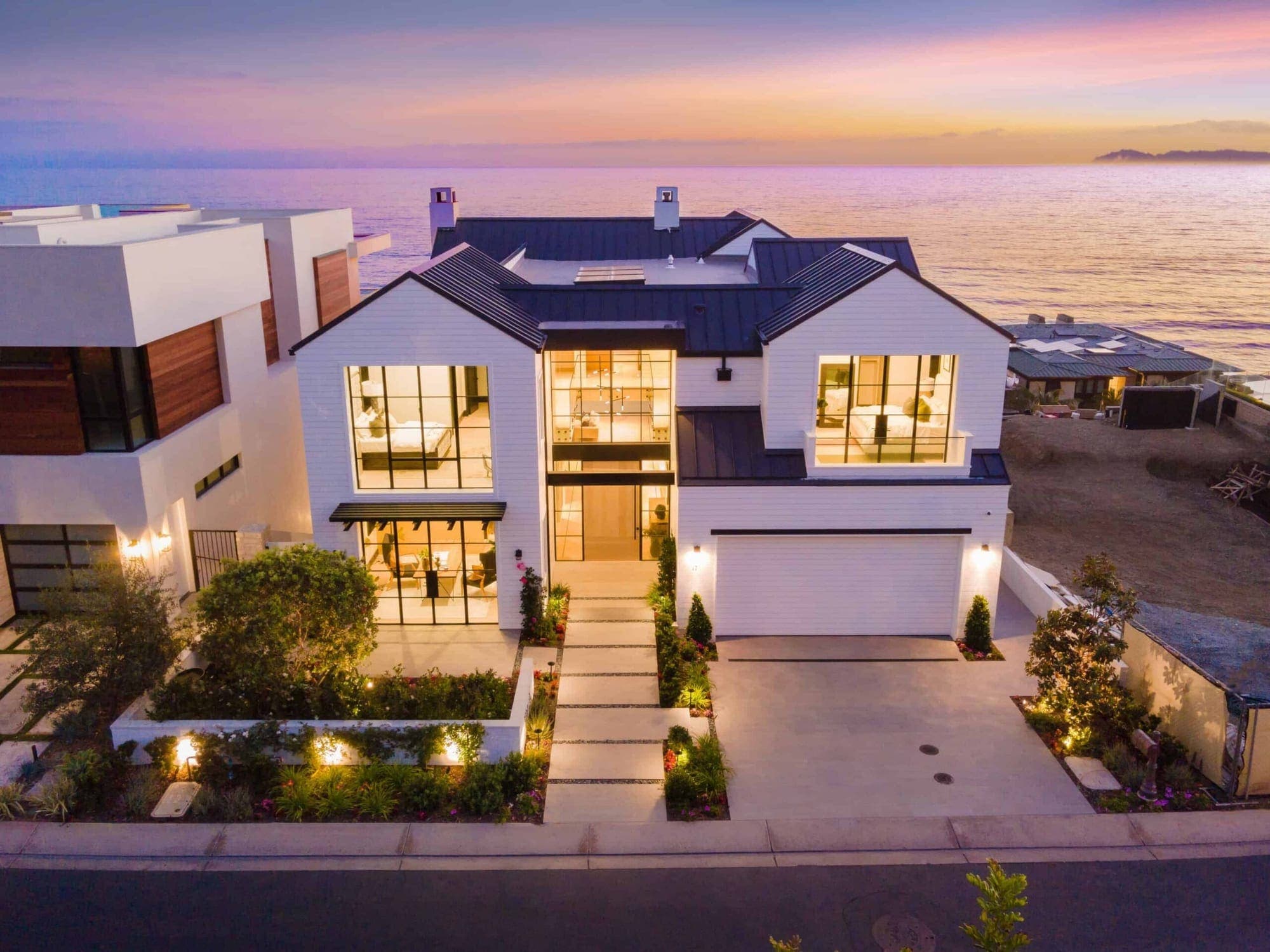 A white oceanfront home in Dana Point at sunset, walls of glass glowing warm above the Pacific.