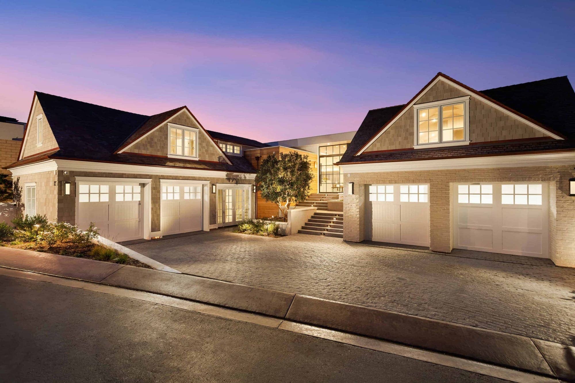 A shingled coastal home in Newport Coast glowing warm at dusk with a lantern-lit entry.