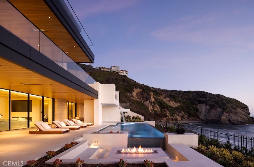 A brand-new contemporary white oceanfront estate at The Strand at Headlands in Dana Point, walls of glass and warm wood opening to terraces, a pool, and the Pacific.