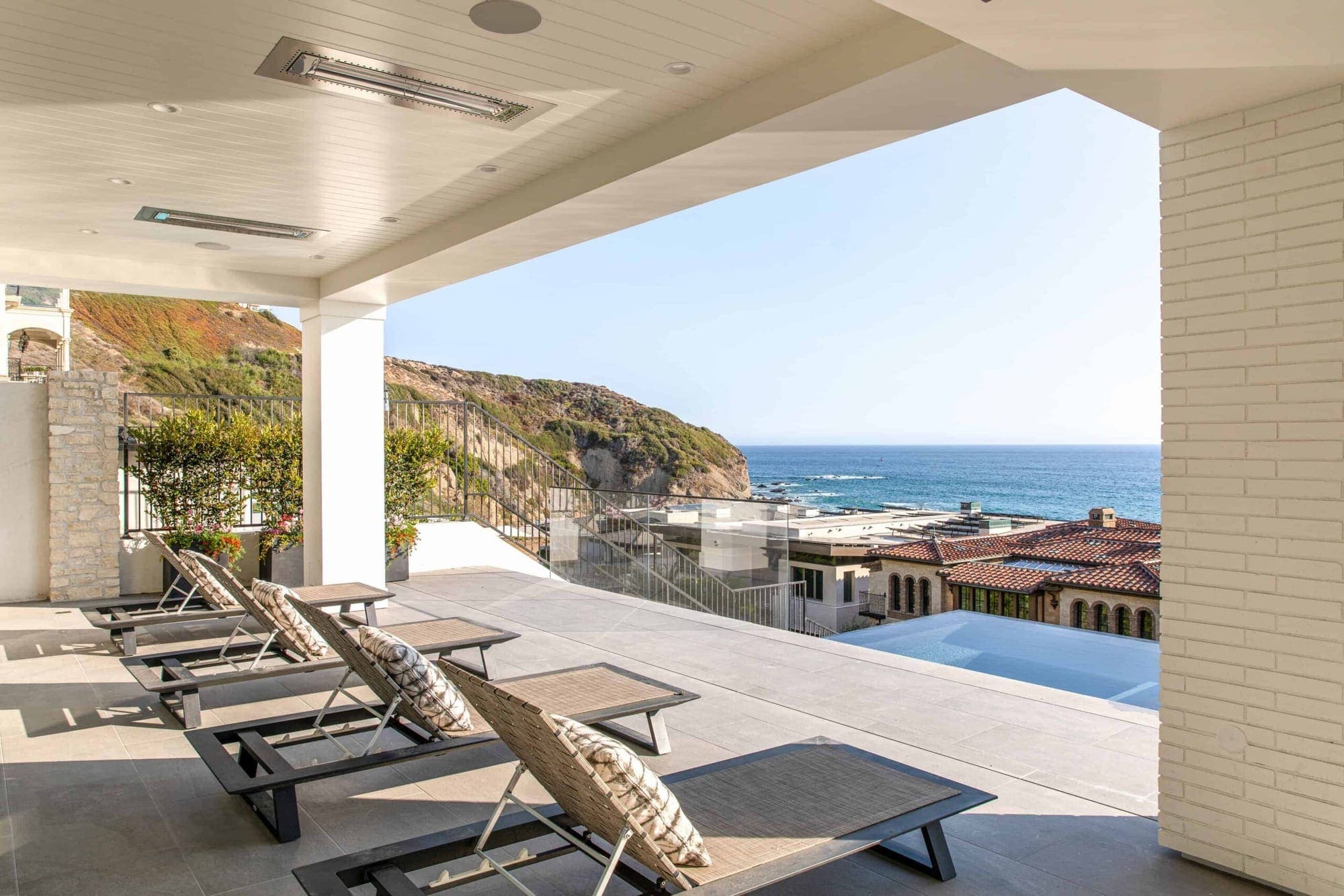 A covered ocean-view terrace lined with sun loungers above the coastline.